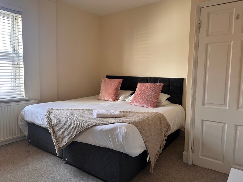 Bedroom with double bed, pink cushions, beige throw, and radiator by window