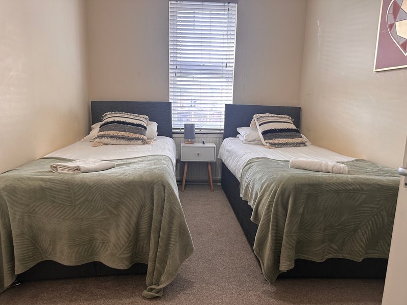 Twin bedroom with two single beds, striped pillows, olive bedcovers, and small bedside table