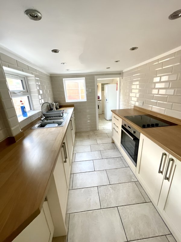 Modern galley kitchen with white cabinetry, wooden worktops, integrated oven and tiled flooring
