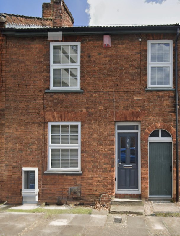 Red brick terraced house with white-framed windows, dark blue door, and stone pathway