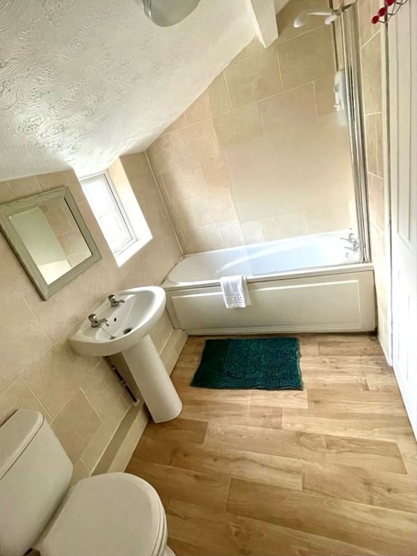 Bathroom with pedestal sink, toilet, bathtub with shower screen and wooden flooring