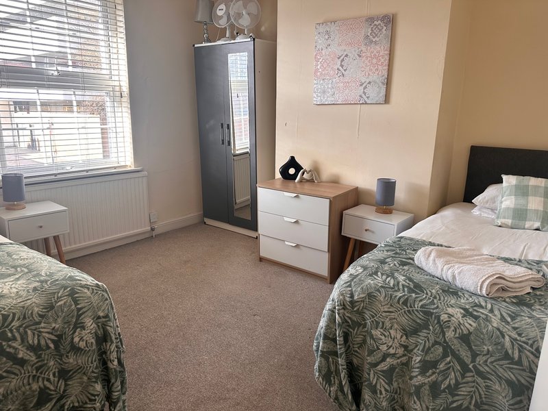Shared bedroom with two single beds, white drawers, radiator and window with blinds