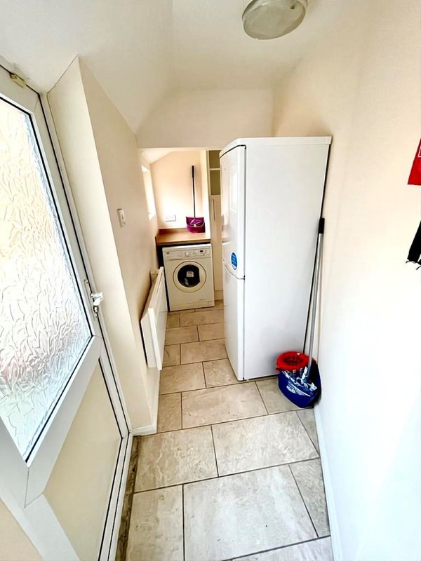 Narrow hallway with washing machine, white fridge, and tiled flooring