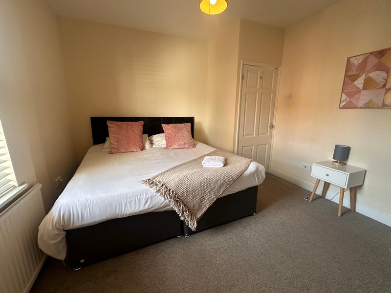 Bedroom with black bed, pink cushions, white bedding, small desk and warm lighting