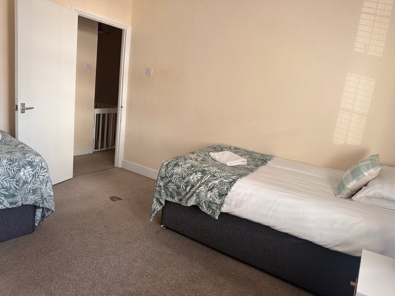 Bedroom with two single beds, patterned bedding, white door and cream walls