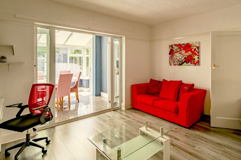 Bright living room with red sofa, glass coffee table, office chair and patio doors
