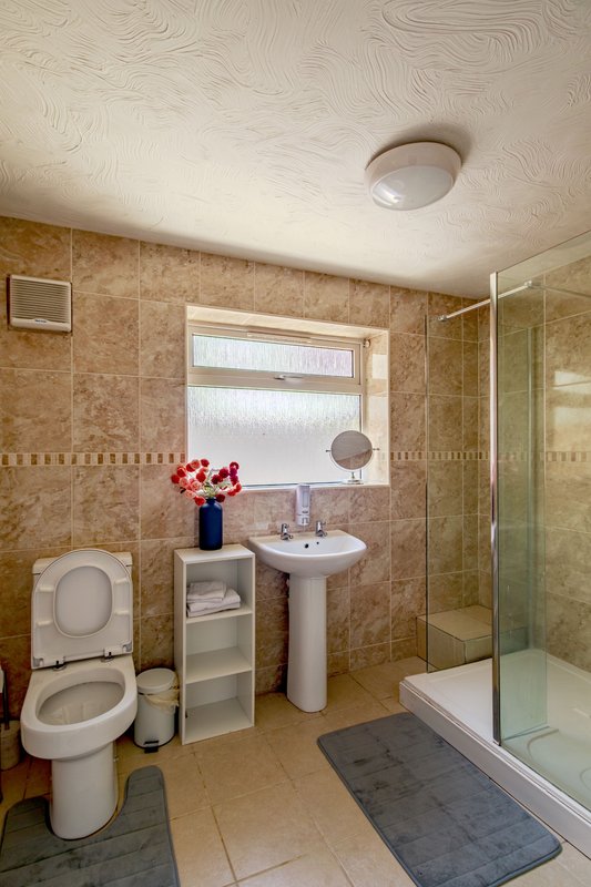 Bathroom with toilet, pedestal sink, shower enclosure, and window with natural light