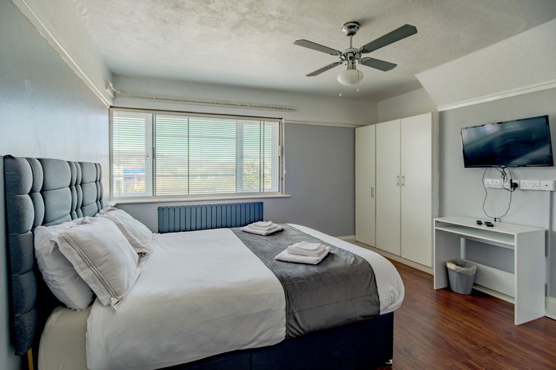 Modern bedroom with double bed, white wardrobes, wall-mounted TV, ceiling fan and large windows