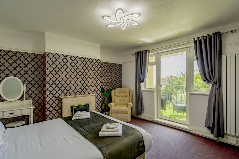 Spacious bedroom with double bed, armchair, patterned headboard wall and garden views