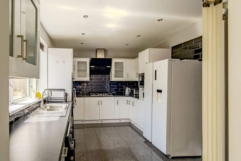 Modern kitchen with white cabinetry, black tile backsplash, stainless steel appliances and gray flooring