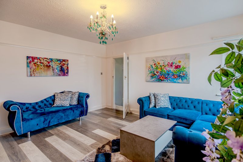 Bright living room with two blue velvet sofas, crystal chandelier, colorful wall art and potted plants