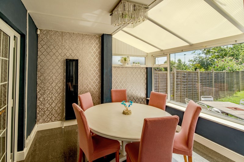 Modern dining room with round white table, coral upholstered chairs, and glass conservatory extension overlooking garden