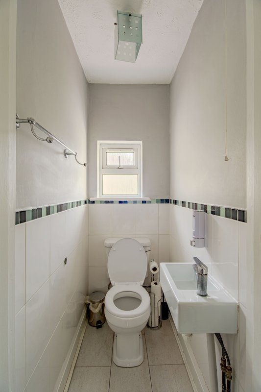 Narrow bathroom with toilet, small sink, tiled walls and small window