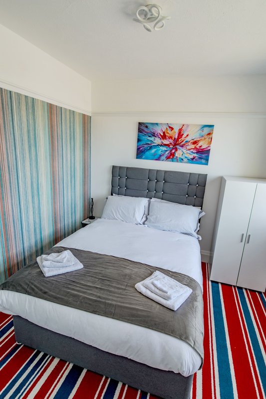 Bright bedroom with gray upholstered bed, colorful artwork, striped curtains and rug