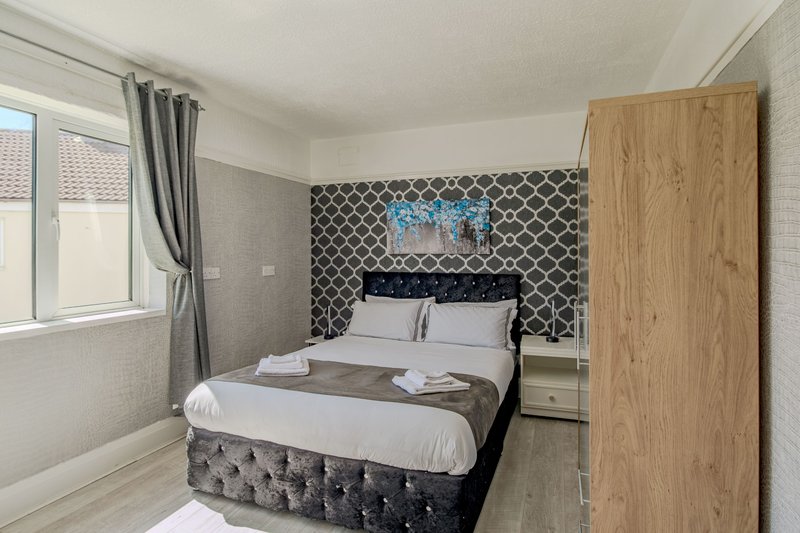 Modern bedroom with double bed, patterned headboard wall, wooden wardrobe and window