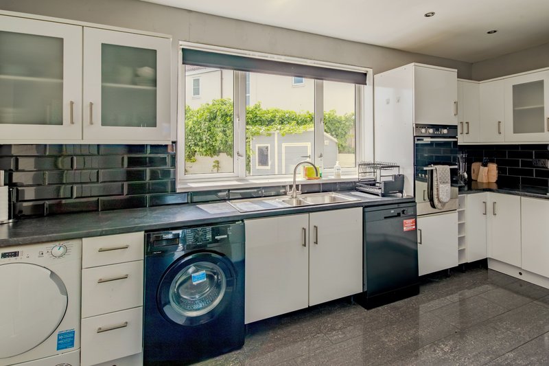 Modern kitchen with white cabinetry, dark countertops, integrated appliances and garden view
