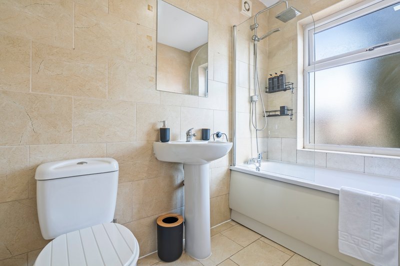 Clean bathroom with toilet, pedestal sink, bathtub, mirror and window