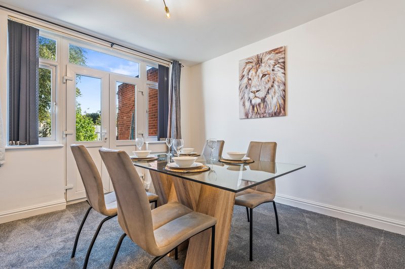 Modern dining room with glass table, wooden base, beige chairs and large windows overlooking garden