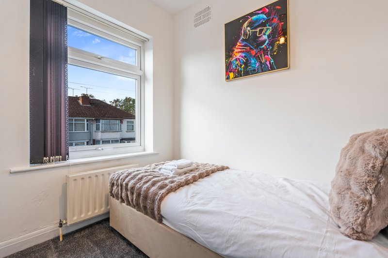 Bedroom with single bed, window overlooking street, radiator and colorful wall art