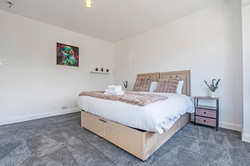 Bright bedroom with double bed, beige headboard, gray carpet, and bedside table with decor