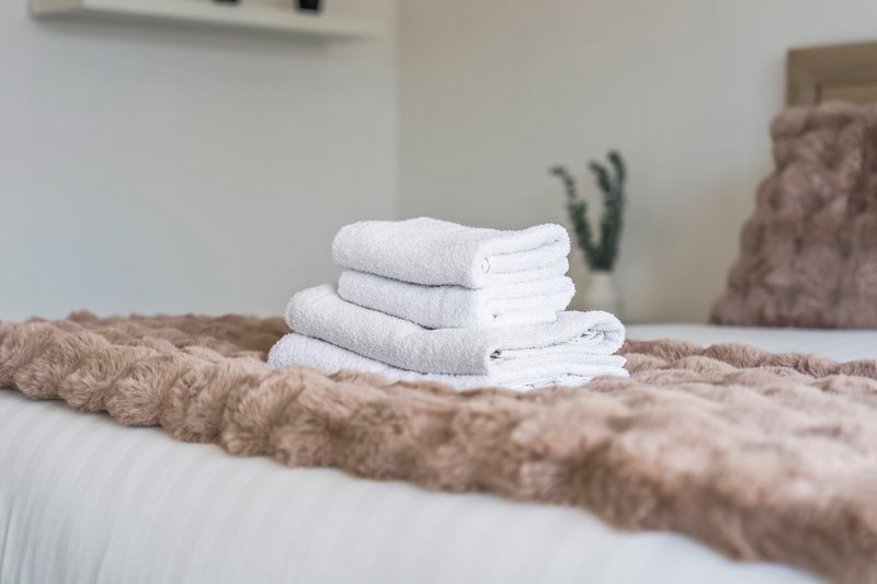 Bedroom with folded white towels on bed, beige bedding and furnishings visible
