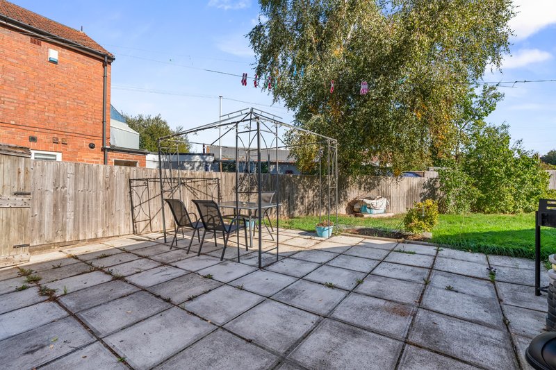 Garden patio with paving stones, metal pergola, chairs and brick house exterior
