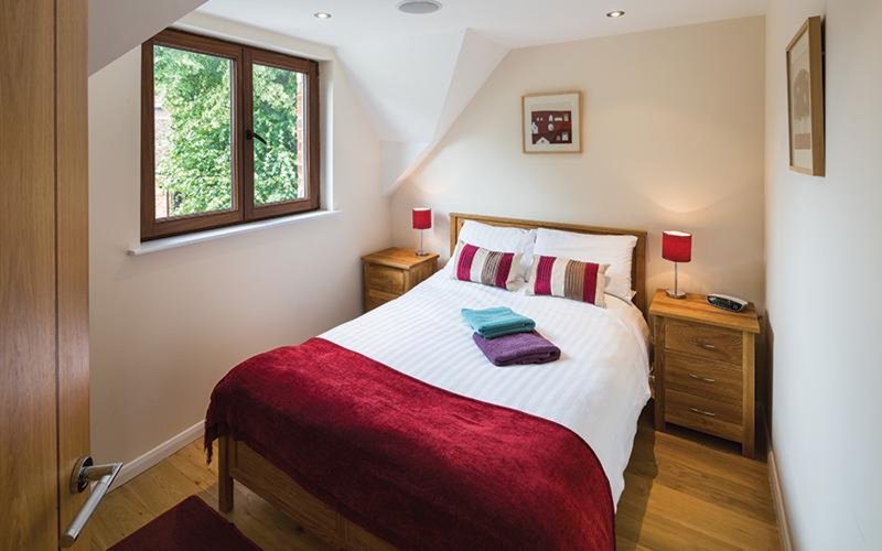 Bright attic bedroom with double bed, burgundy throw, wooden furniture and sloped ceiling
