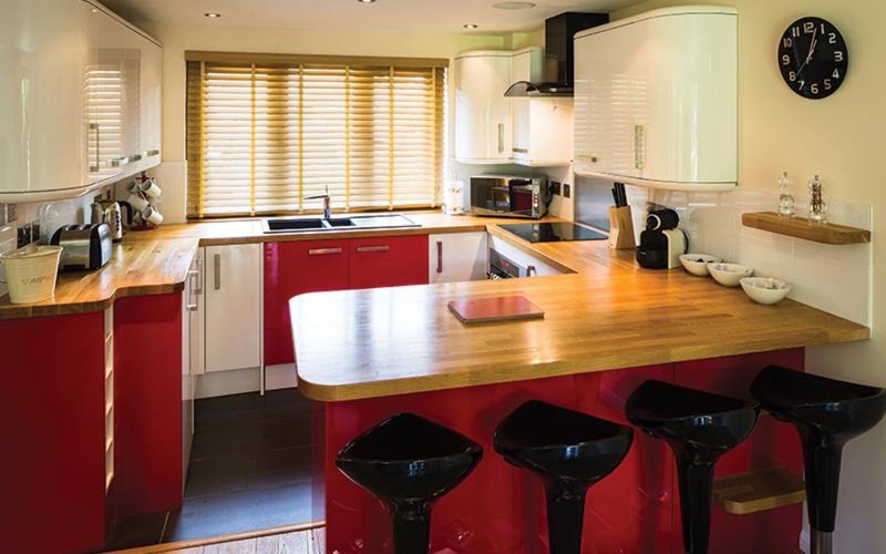 Modern kitchen with red and white cabinetry, wooden countertop, island with bar stools, and window with blinds