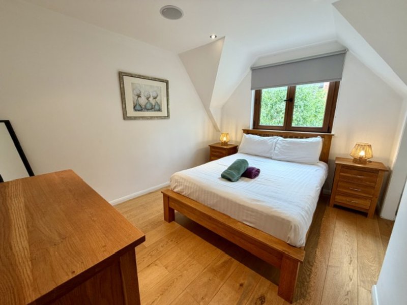 Bright attic bedroom with double bed, wooden furniture, desk, and sloped ceiling