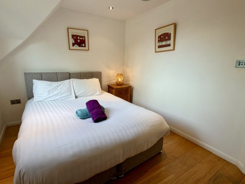 Attic bedroom with double bed, grey headboard, wooden floor, and wall art
