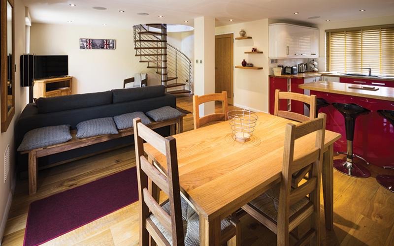 Open-plan living area with dining table, black sofa, kitchen, and stairs