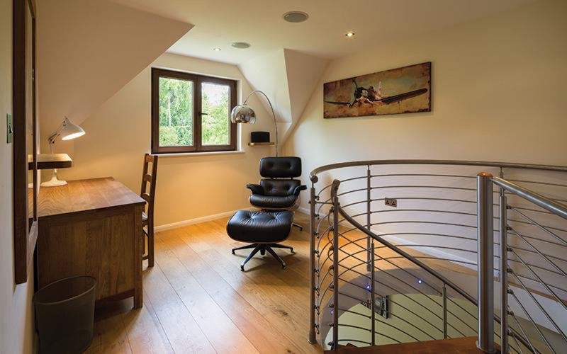 Modern loft bedroom with double bed, office chair, desk, metal railing and sloped ceiling