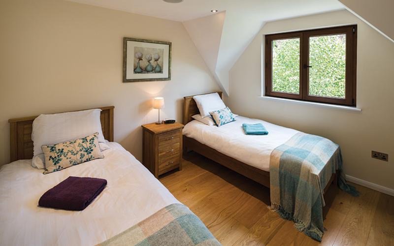 Bright attic bedroom with two single beds, wooden nightstand, framed artwork and window