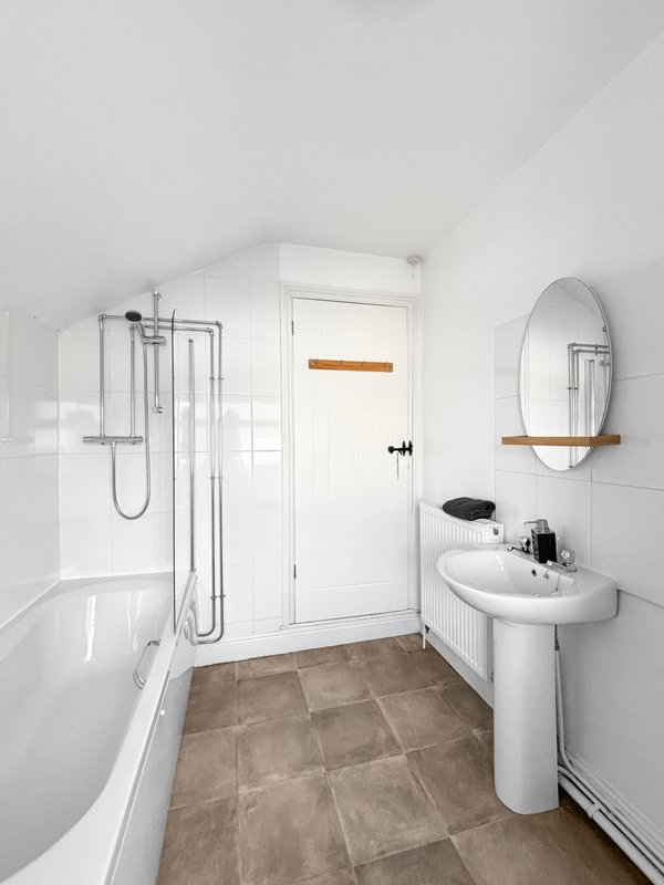 Clean bathroom with bathtub, shower enclosure, pedestal sink and circular mirror