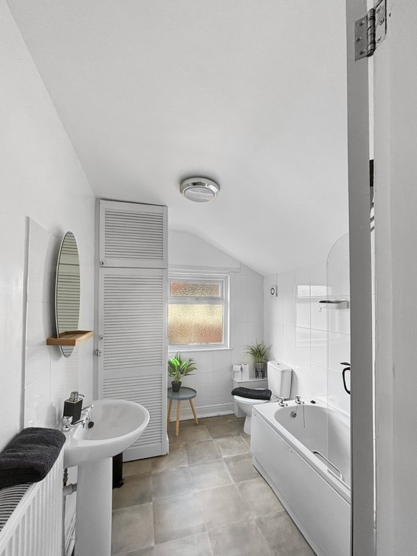 Modern bathroom with white tiles, sink, toilet, bathtub and window
