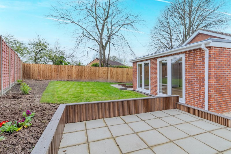 Modern brick extension with patio, garden and wooden fence in bright daylight
