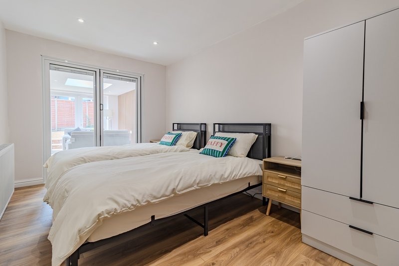 Modern bedroom with two single beds, wooden flooring, wardrobe and glass balcony doors