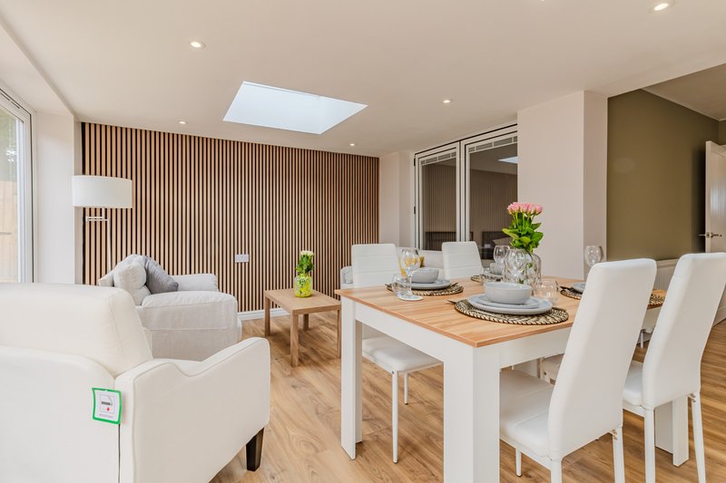 Open-plan living and dining area with wooden flooring, dining table, white chairs, and seating area