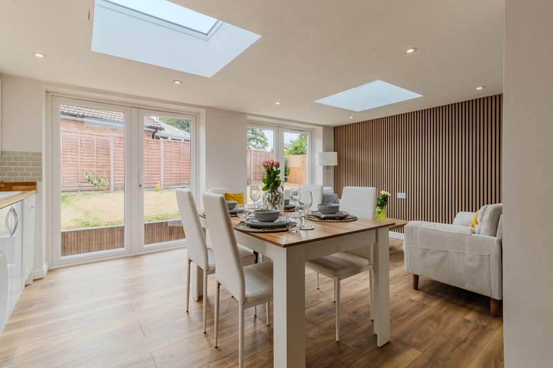 Open-plan dining and living area with wooden table, chairs, sofa, skylights and patio doors