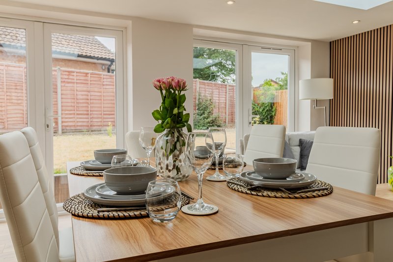 Modern dining room with wooden table, place settings, fresh flowers and garden views
