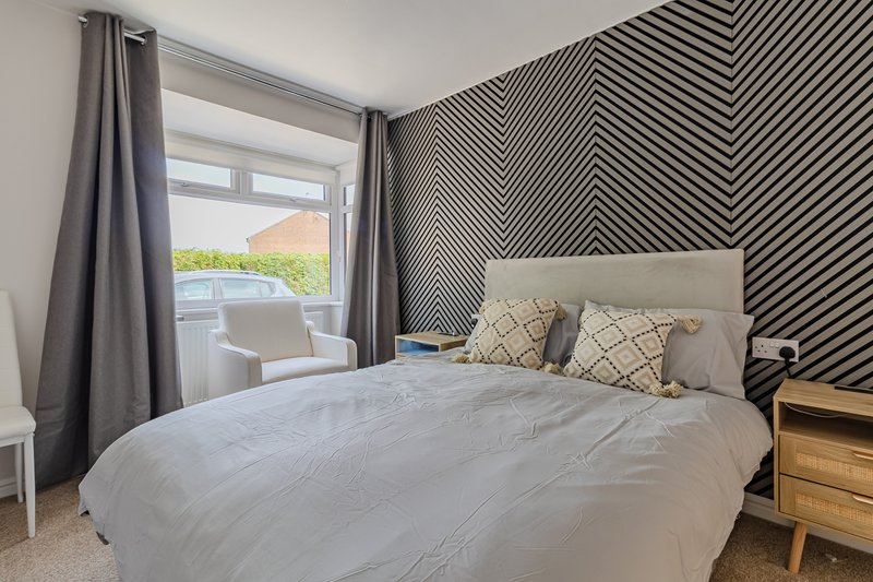 Modern bedroom with double bed, geometric accent wall, wooden nightstand and garden view