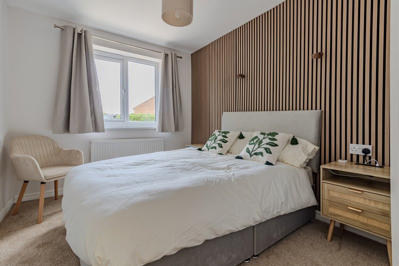 Modern bedroom with double bed, wooden slat accent wall, and natural light from window