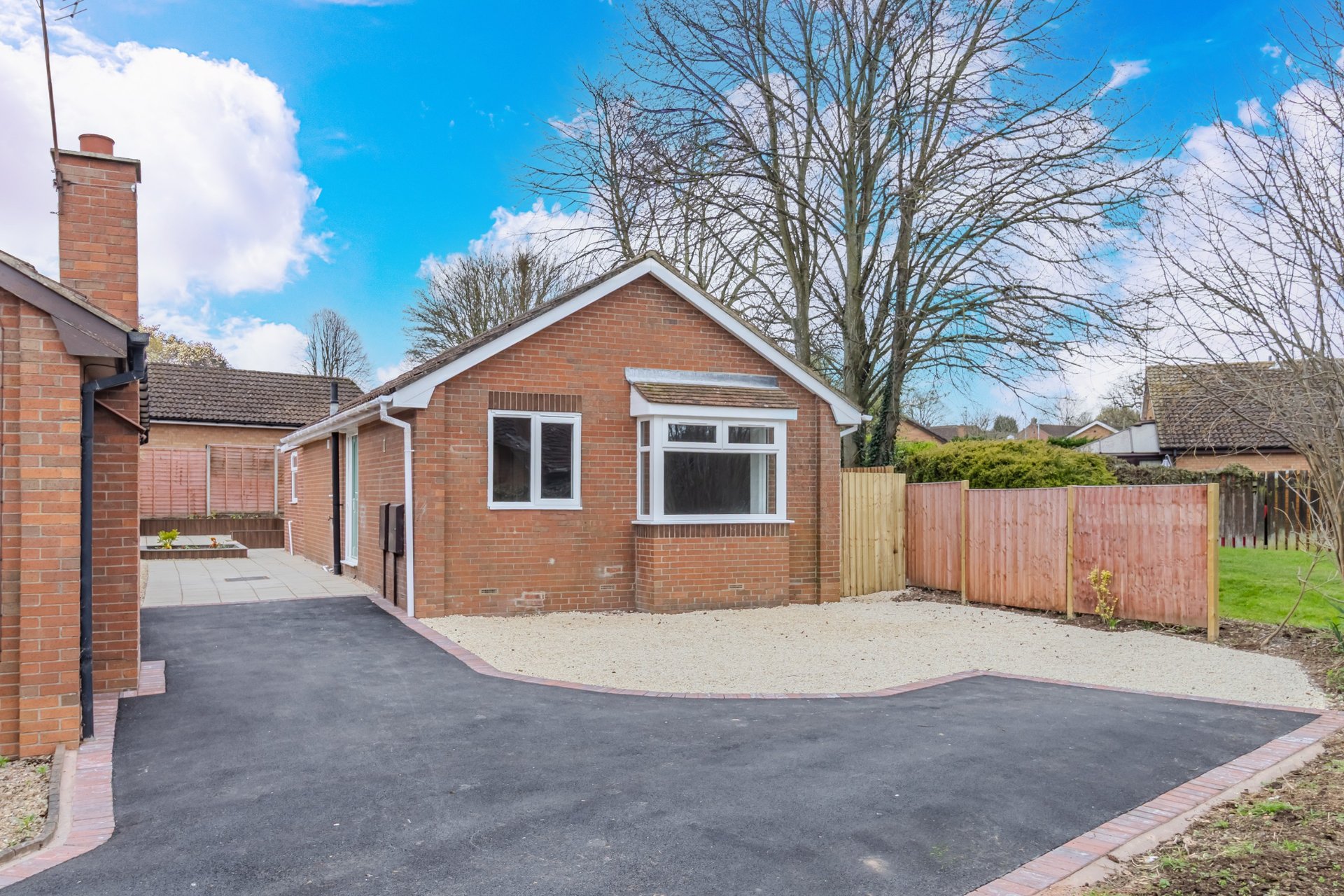 Brick bungalow with driveway, garage, and wooden fence surrounding property