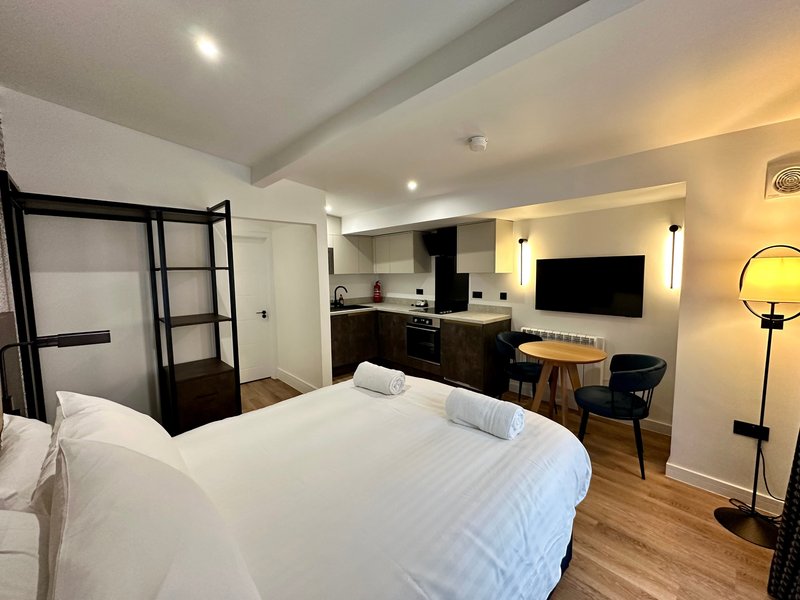 Modern studio apartment with bed, kitchenette, desk area and wall-mounted TV