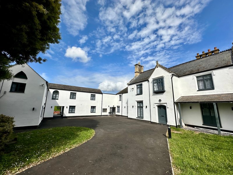 White-rendered country property with courtyard, driveway, manicured lawn and clear sky