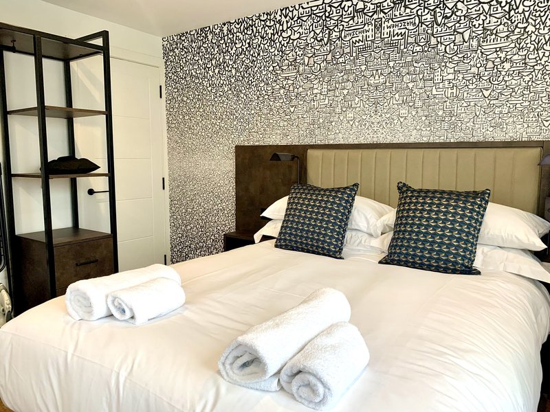 Modern bedroom with double bed, patterned headboard, rolled towels, and geometric wallpaper