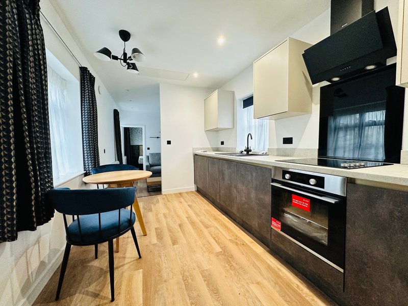 Modern kitchen with dark cabinetry, wooden flooring, dining area and ceiling fan