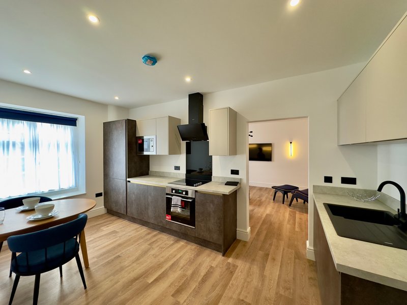 Modern open-plan kitchen and dining area with wooden flooring, fitted cabinetry, and breakfast bar