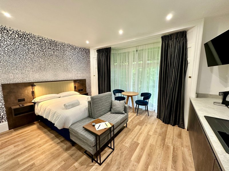Modern bedroom with double bed, seating area, desk, and large windows with dark curtains