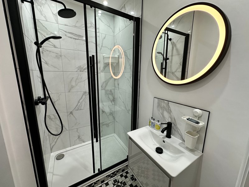 Modern bathroom with walk-in shower, white sink, illuminated mirror and grey floor tiles